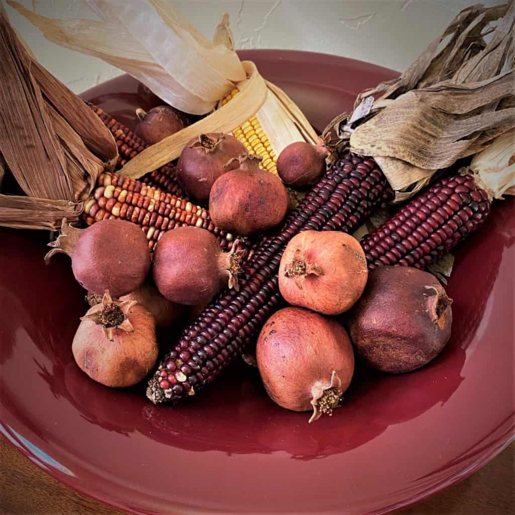 crimson bowl of dried corn and pomegraantes decorate a Thanksgiving table