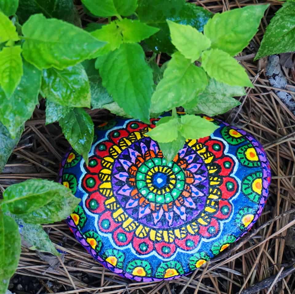 intricately painted rock in a garden bed