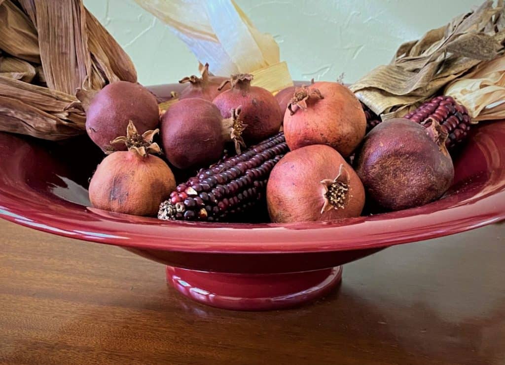 close-up of dried pomegranates and red corn in crimson bowl decorating Thanksgiving table